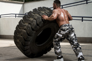 A muscular man participating in a cross fit workout by doing a tire flip